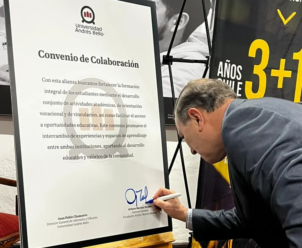 Man signs a framed document titled 'Convenio de Colaboración' on a wooden easel at an event, with the Universidad Andrés Bello logo visible.