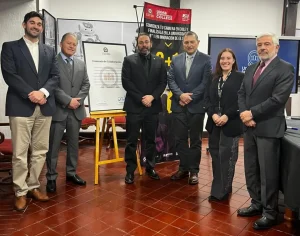 Six professionals in business attire posing for a photo at a collaboration event, with an agreement framed on an easel and banners in the background.