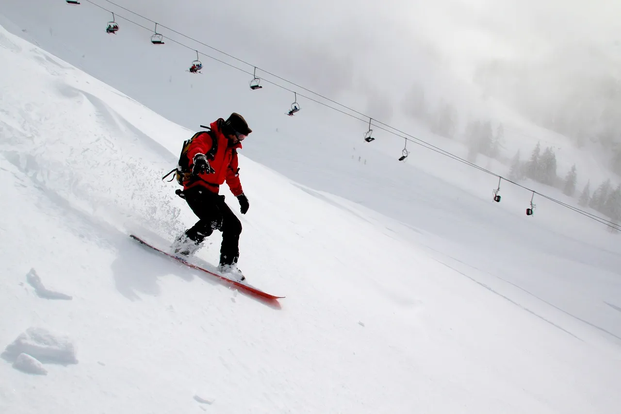 Skier in a red jacket carving down a snowy slope with a chairlift in the background.