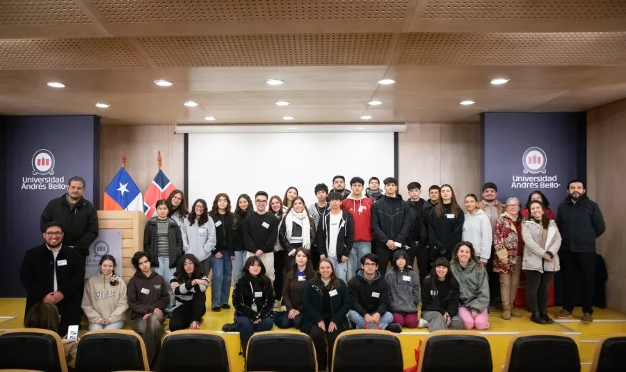 Group of students and staff posing on a stage in a university auditorium, with Chilean flags and banners on sides.