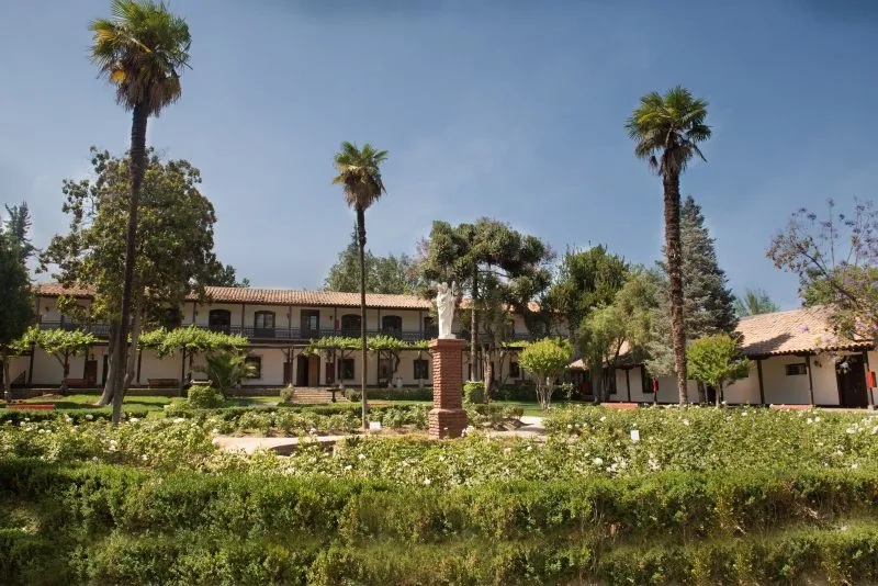 Courtyard of a campus with a statue on a brick pedestal, palm trees, and a two-story building in the background.
